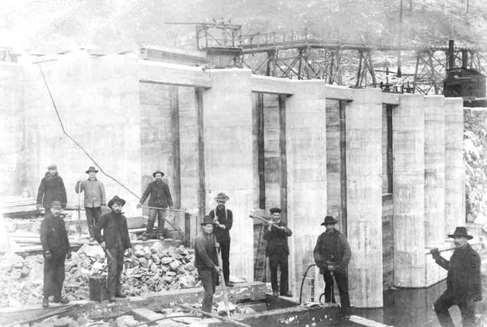 Workers in front of the immense dam structure during the early construction ages.