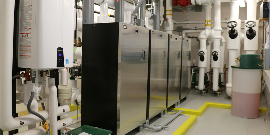 : A row of boilings and a tankless water heater in the boiler room of a school.