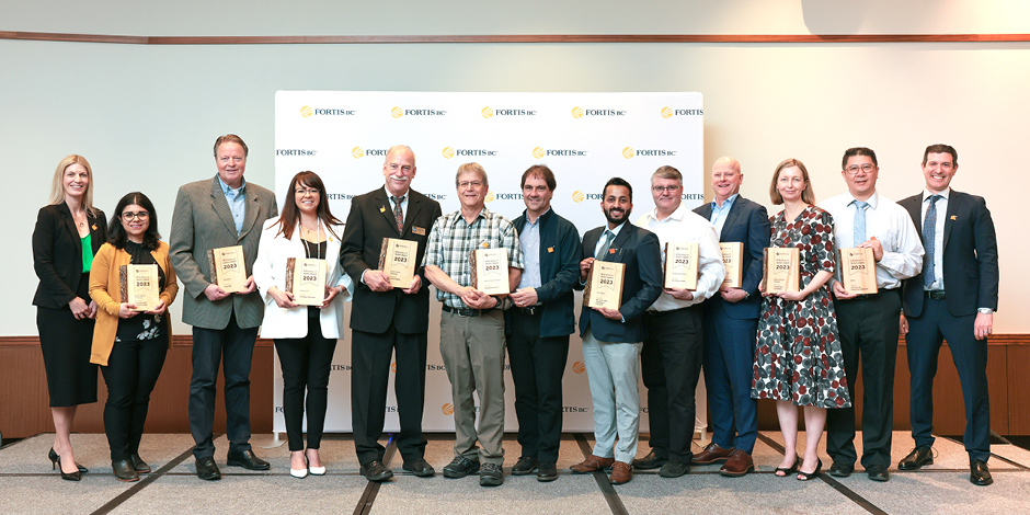 Group of people standing in front of a backdrop with FortisBC logo and holding wooden award plaques for the 2023 Efficiency in Action Awards.