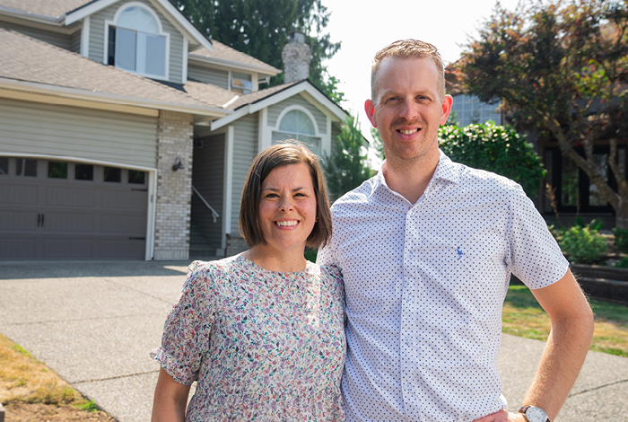 A couple smiling, standing together on the driveway in front of their home.