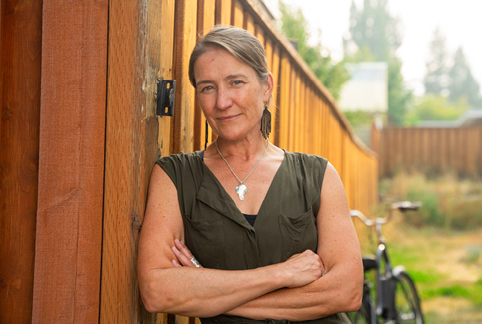 A woman smiling, leaning against a fence in her backyard.