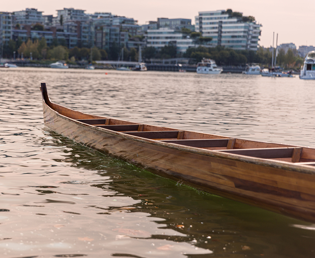 A modern Coast Salish racing canoe floating in False Creek with Vancouver skyline in background.