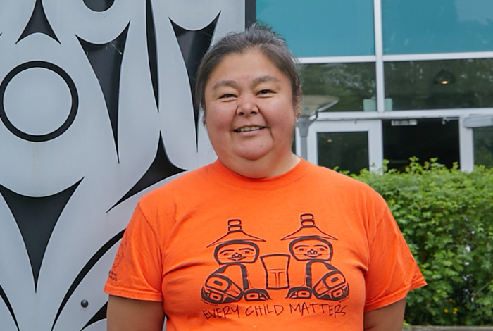 A smiling women in orange t-shirt in front of an Indigenous sculpture.