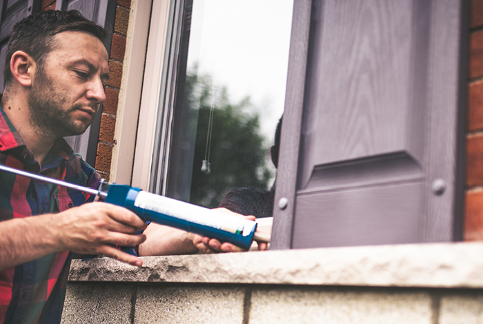 Man applies caulking to exterior side of a window on a brick house