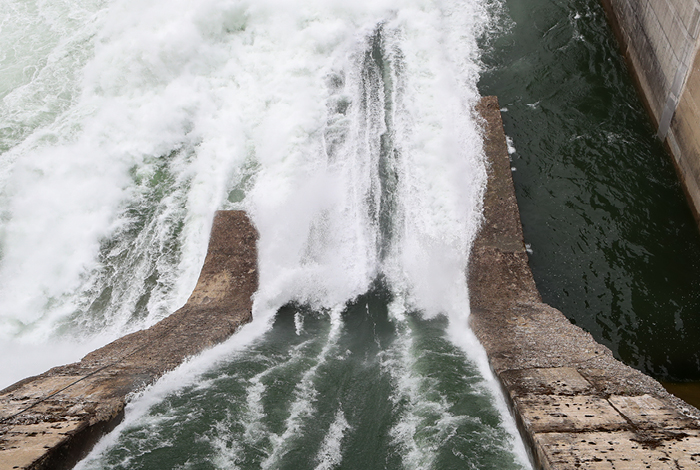 Looking from above, water is forcefully rushing down over the spill gate of a FortisBC hydroelectric dam