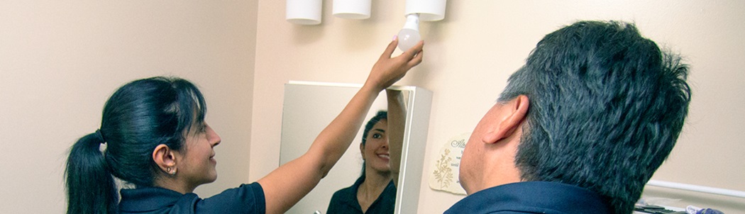 A women changing a bathroom vanity lightbulb to an energy-effcient LED one while a resident watches.