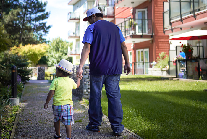 A father and small toddler walk together near a nieghbourhood condominium complex.