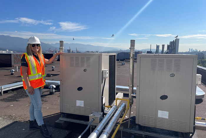 A woman standing beside two gas absorbtion heatpumps.