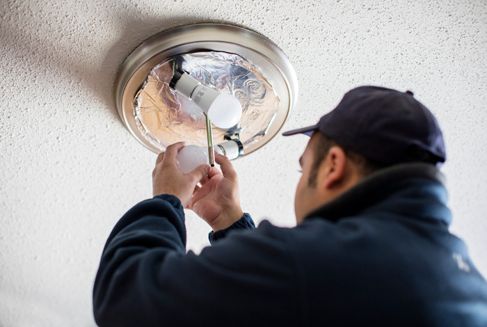 A handyman installing an energy-efficient LED light bulb in an overhead lighting fixture.