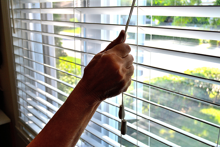 A person's hand closing horizontal blinds to keep their home cool.