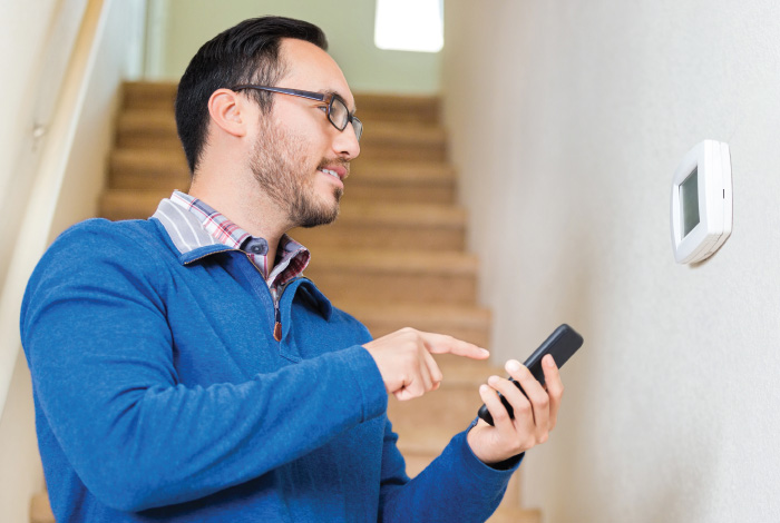 man using his smart phone to program his home’s thermostat