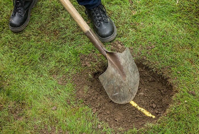 A person digging a hole with a shovel and carefully reveling a yellow gas line