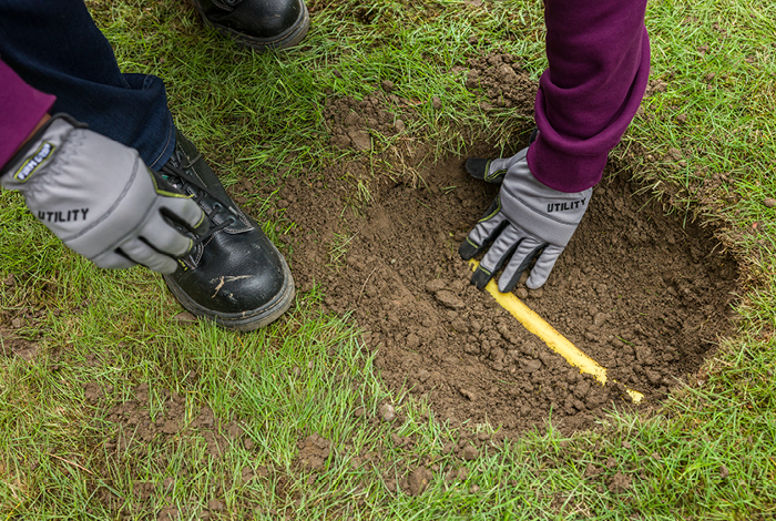 A person using their gloved hand to carefully reveling a yellow gas line