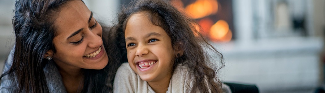 Mother and daughter laying on a living room floor, laughing together with a gas fireplace in the background