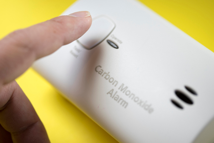 A person about to press the test button on a carbon monoxide alarm.