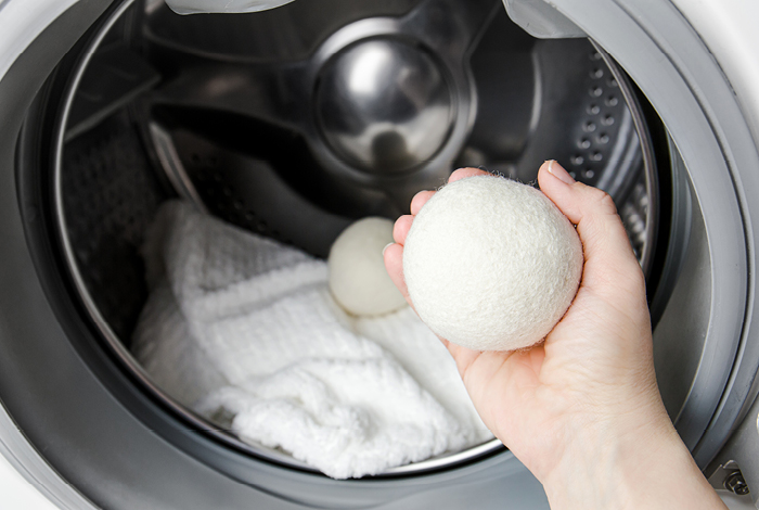 A person putting a white dryer ball in the machine with a white blanket.