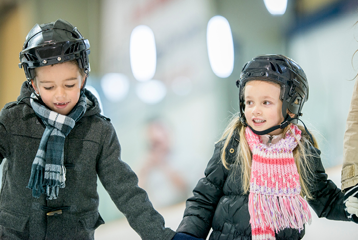 Two children skating together at a community arena.