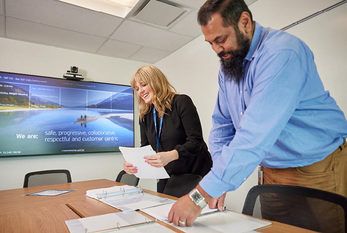 Two employees in a meeting room, working together on paperwork.