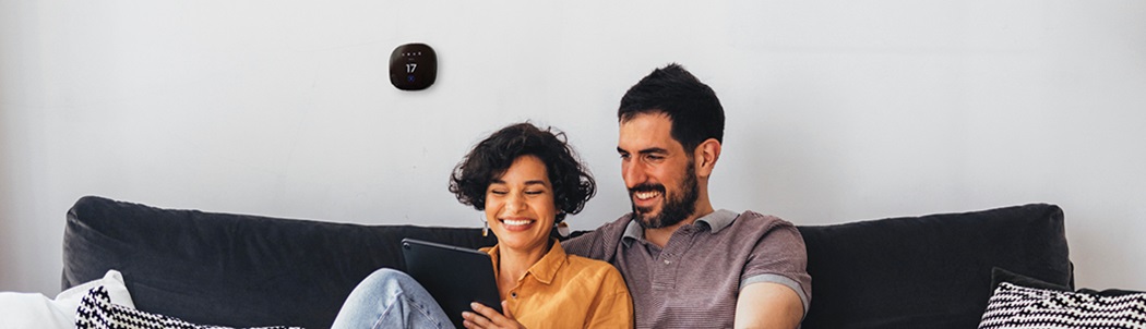 A smiling couple looking at a tablet together in front of a programmable thermostat