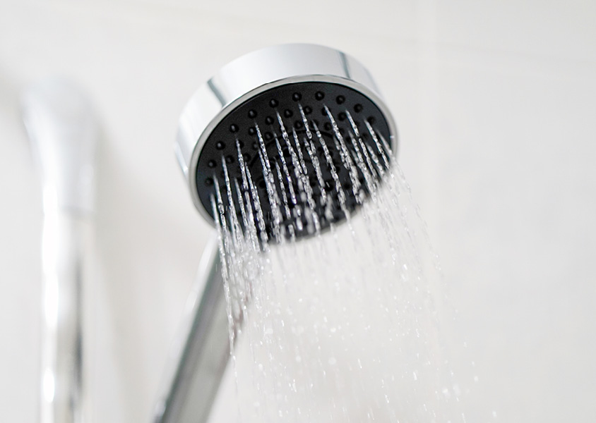 A bathroom shower head spraying water.