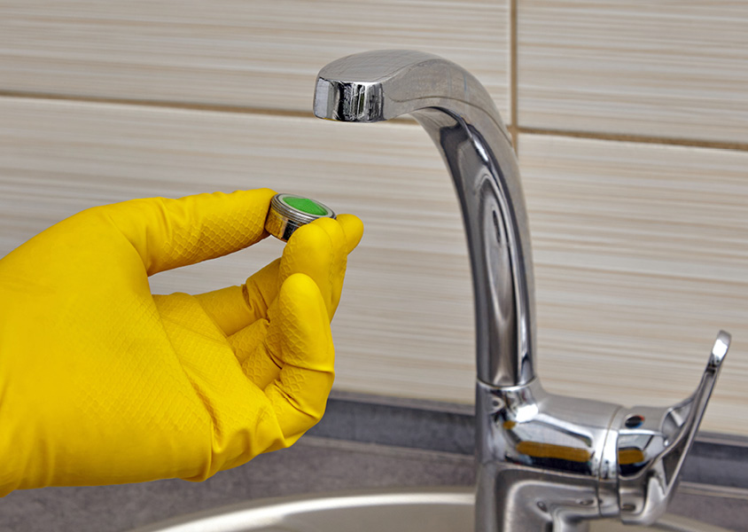 A close-up of a hand in a kitchen installing a faucet aerator.