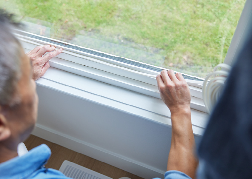 A person installing weatherstripping along a windowframe.