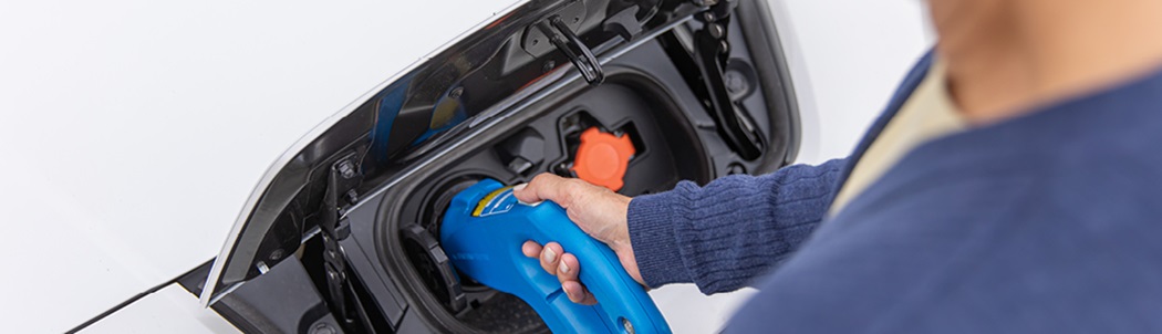Woman plugging in the connector into her electric vehicle’s charging port.