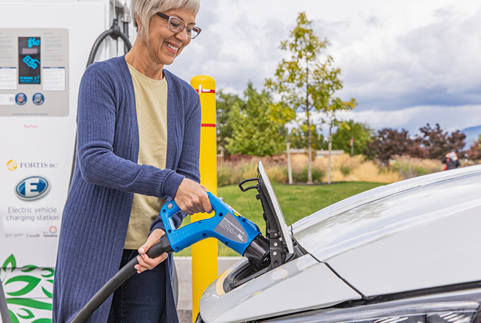 Woman plugging in the charging stations connector into her electric vehicle’s charging port.