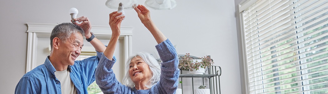 Two people replacing an old incandescent lightbulb with a new energy-efficient LED bulb.