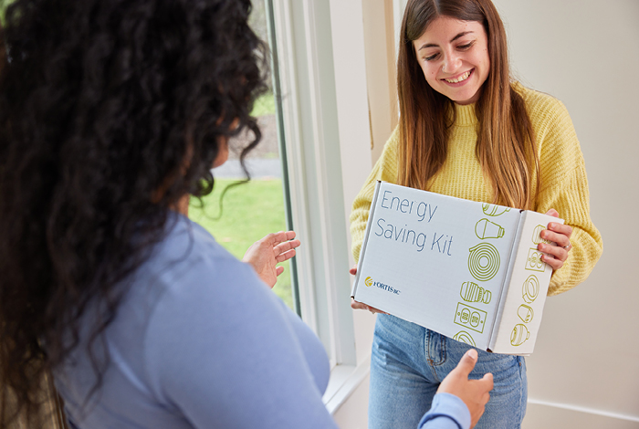 A teenage girl proudly presenting an Energy Saving Kit box to her mother.