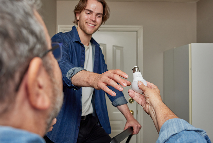 A grandfather handing an LED light bulb to his grandson so he can help install it.