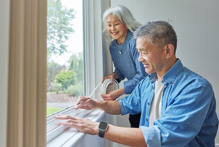A senior couple working together to install foam weather stripping to their window frame