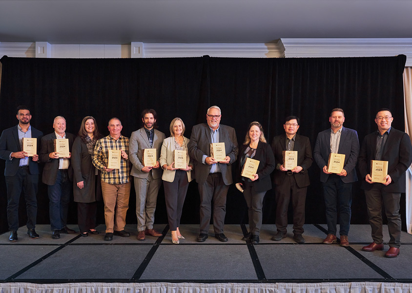 Group of people standing in front of a backdrop with FortisBC logo and holding wooden award plaques for the 2024 Efficiency in Action Awards.