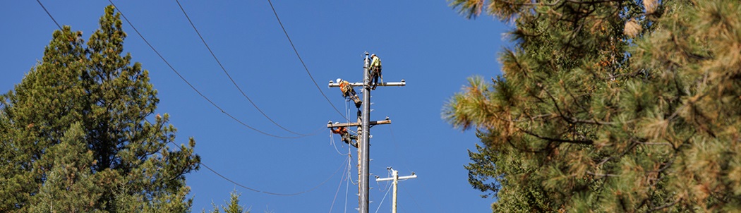 Three utility workers wearing safety gear are patrolling a power pole to make sure it’s safe to restore electricity.