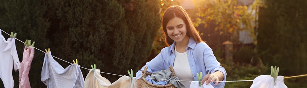 Lady smiling while hanging laundry on a clothing line in a sunny garden.