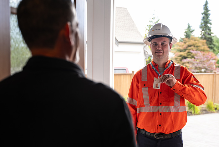 A gas meter technician stands in a doorway as a resident greets him. The gas meter technician is showing his FortisBC ID.