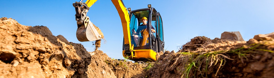 Yellow excavator digging a trench at a construction site. Always click or call before you dig.