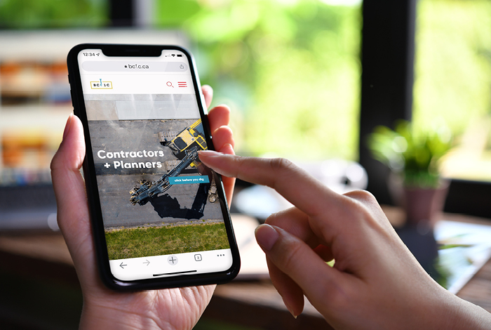 A person holding a smartphone showing the BC 1 Call website for contractors and planners, used to request underground utility locates before digging.