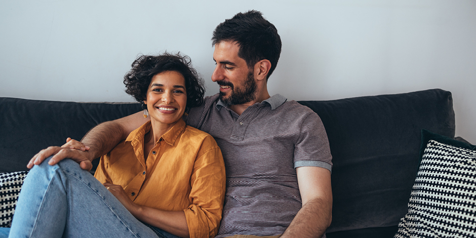 A woman wearing an orange shirt sitting next to a man wearing a grey shirt.