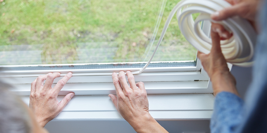Two individuals weatherstripping a window.