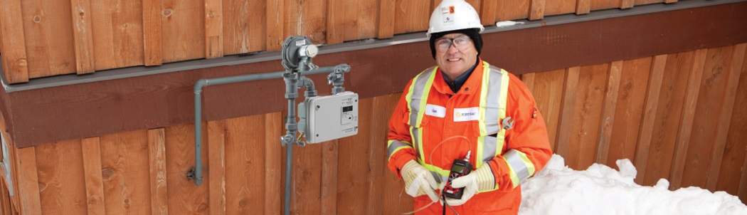 Gas meter technician beside a new meter in wintertime at the side of a residential property.