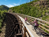 Two people riding their bikes across a trestle.