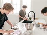 Three teenage boys are in a kitchen making bread, shopping vegetables and working on a tablet