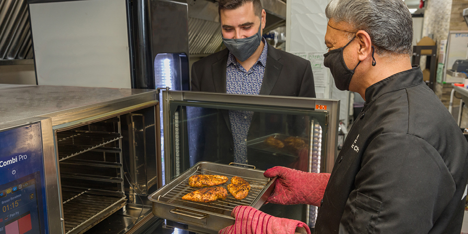Tiago Pereira, FortisBC energy solutions manager, looks on as Lucky removes chicken from his new combination oven.