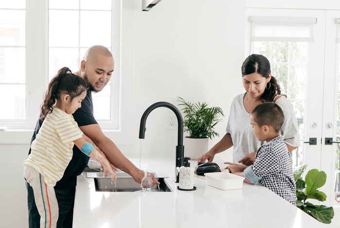 Family standing over the sink washing dishes.