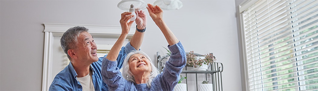 Elderly couple smiling as they install LED bulbs in their ceiling fixture.