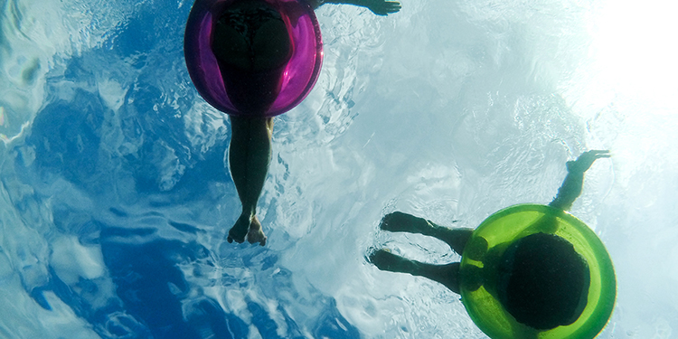Underwater photo showing two people floating on inner tubes with legs dangling in water.